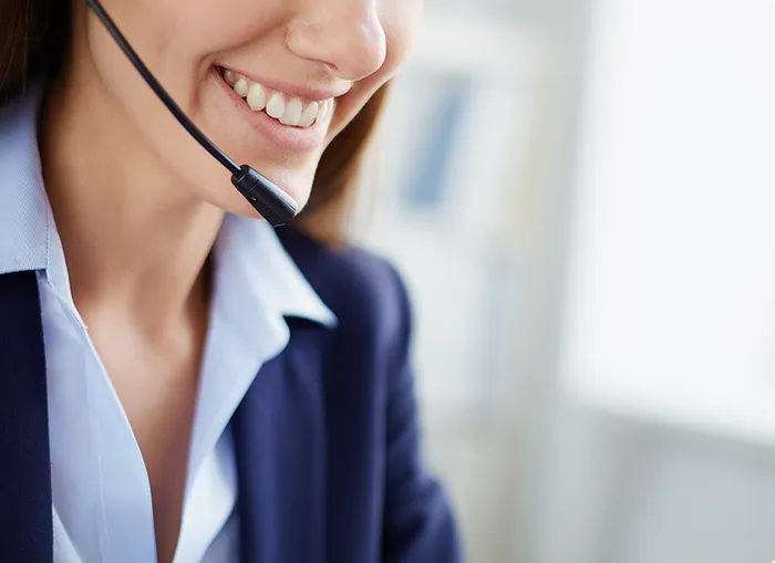Close-up of a smiling person wearing a headset with a microphone, dressed in professional business attire, likely engaging in a customer service or sales call
