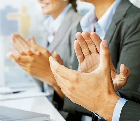 Close-up of several people in business attire clapping their hands in applause, likely during a training session, presentation, or meeting